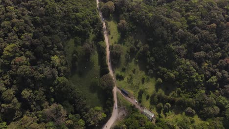 Slow-motion-aerial-drone-footage-of-cars-driving-through-a-dirt-road-in-a-tropical-rainforest-rural-landscape,-in-Monteverde,-Costa-Rica