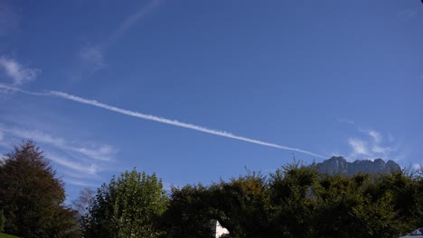 Contrail-with-blue-sky-and-alpine-mountains-near-the-town-of-Annecy,-Wide-locked-shot