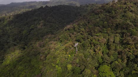Cinematic-aerial-drone-footage-of-sky-tram-gondolas-traveling-up-hill-in-a-tropical-forests-in-Costa-Rica,-Monteverde