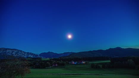 Toma-Estática-Amplia-De-Un-Paisaje-Pintoresco-En-Austria-Por-La-Noche-Con-Un-Intenso-Cielo-Azul-Con-Luna-Llena-Sobre-Las-Majestuosas-Cadenas-Montañosas-Y-Densos-Bosques-Con-Prados
