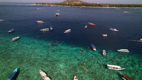 Many-Tourists-Snorkeling-at-Gili-Statues-with-Tour-Boats-Moored-in-Tropical-Blue-Ocean-near-Trawangan-Island-in-Indonesia---Aerial-Orbit-View