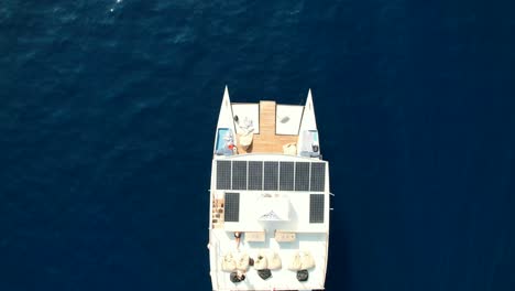 Aerial-Top-Down-View-of-Modern-Catamaran-Yacht-Cruising-in-Blue-Sea-and-Couple-Suntanning-on-the-Rooftop