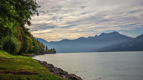 Timelapse-from-the-shore-of-the-beautiful-attersee-lake-with-a-view-of-the-calm-waters-reflecting-the-fast-moving-clouds-and-majestic-alpine-peaks-in-the-background-on-a-cold-fall-morning