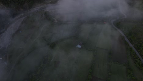 Aerial-view-from-a-drone,-looking-down-at-the-fog-covered-valley-with-Benja-Thermal-Baths-and-the-Vjosa-River-in-Albania