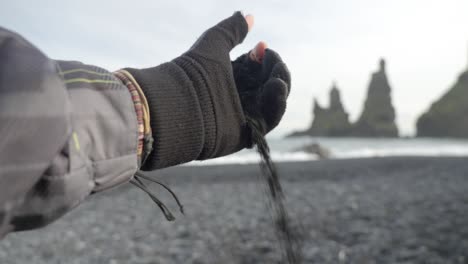 close-up-hand-with-glove,-falling-black-sand-on-black-sand-beach-in-Iceland