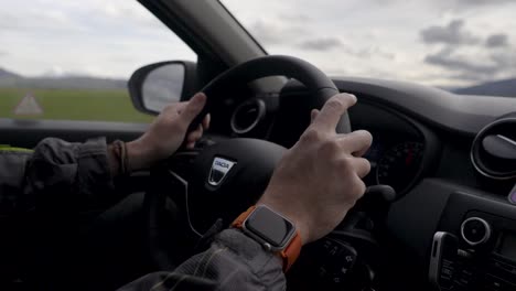Man-driving-the-car-while-driving-through-scenic-landscape-in-Iceland,-hands-on-the-steering-wheel