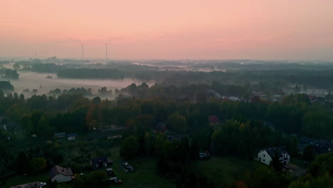 Foggy-Polish-township-with-wind-turbines-during-sunrise,-aerial-view