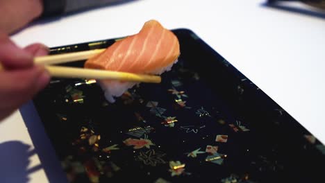 Last-piece-of-sake-nigiri-sushi-is-plucked-from-plate-with-chopsticks