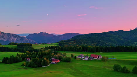 Panoramaaufnahme-Eines-Landes-Mit-Bäumen-Und-Wenigen-Häusern,-Sichtbare-Berge-In-Der-Ferne-Mit-Rosafarbenem-Himmel