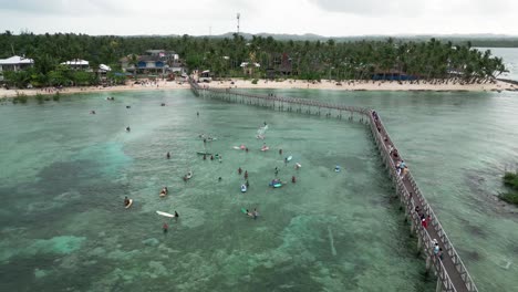 Drone-shot-of-Siargao-wooden-Boardwalk-and-people-surfing,-Philippines