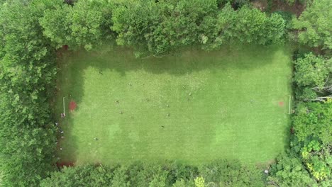 Aerial-view-of-a-lush-green-soccer-field-surrounded-by-trees-with-a-soccer-match-in-progress