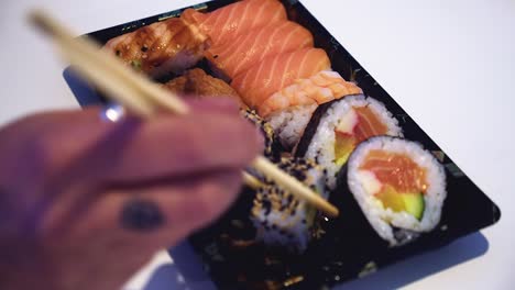 Defocused-hand-picks-sushi-roll-from-assorted-platter-with-chopsticks