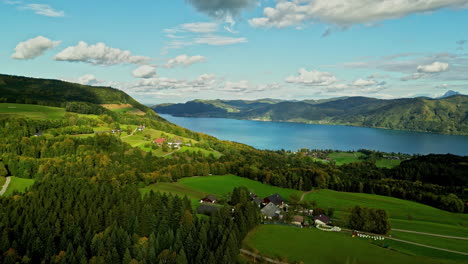 Aerial-capture-of-densely-vegetated-landscape-with-cluster-settlements-and-a-large-water-body-visible-in-the-background-in-Attersee-Austria