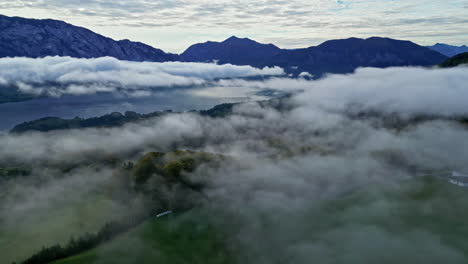 Aerial-view-backwards-over-low-hanging-clouds-at-lake-Attersee,-in-Austria