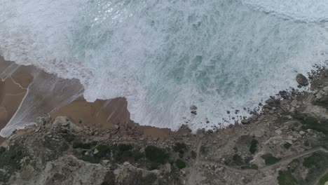 Top-aerial-drone-view-of-waves-crashing-on-rocky-coastline