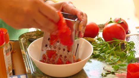 Nahaufnahme-Von-Händen,-Die-Die-Reibe-Halten-Und-Tomaten-In-Kleine-Stücke-Reiben,-Um-In-Einer-Küche-Eine-Paella-Sauce-Namens-Sofrito-Zuzubereiten