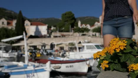 Woman-walking-in-idyllic-seaside-town-promenade-passing-by-boats,-Bol,-Croatia