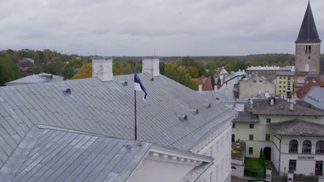 Drone-flying-backwards-away-from-Tartu-university-main-building-and-top-of-it-there-is-Estonian-flag-and-on-background-we-can-see-beautiful-autumn-in-Tartu