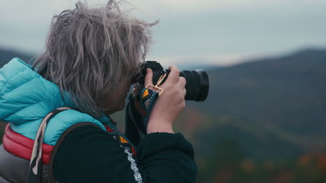 Cinematic-close-up-shot-of-a-woman-photographer-with-grey-hair-taking-pictures-with-her-camera-during-a-windy-day-in-autumn-nature-in-slow-motion