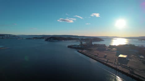 Aerial-drone-forward-moving-shot-over-Oslofjord-Inlet-Waterway-with-sun-rising-in-the-background-in-Oslo,-Norway-during-morning-time
