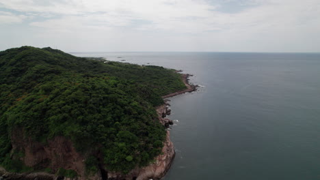 Drone-orbits-from-left-to-right-over-Punta-de-Mita's-rocky-coast,-revealing-mountains-and-sea-in-a-sweeping-view