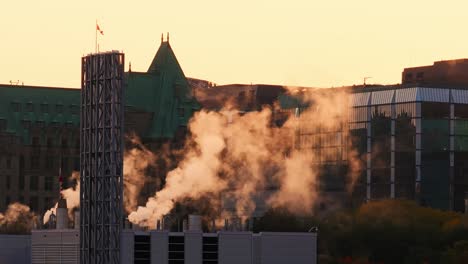 An-Einem-Sonnigen-Morgen-Steigt-Dampf-Aus-Einem-Industriegebäude-In-Der-Innenstadt-Von-Ottawa-Mit-Regierungsgebäuden-Und-Einer-Kanada-Flagge-Im-Hintergrund