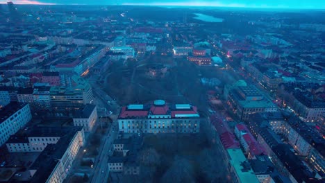 Aerial-drone-backward-moving-shot-over-residential-buildings-surrounding-a-park-in-Stockholm,-Sweden-in-evening-time-blue-hour