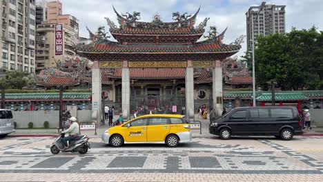 Frontal-view-of-the-famous-Bangka-Longshan-Temple-and-scene-of-slow-moving-traffic-in-Wanhua-District,-Taipei,-Taiwan