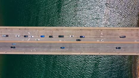 Timelapse-aerial-view-of-San-Diego-freeway-overpass-with-ocean-water-below-and-traffic-passing-by