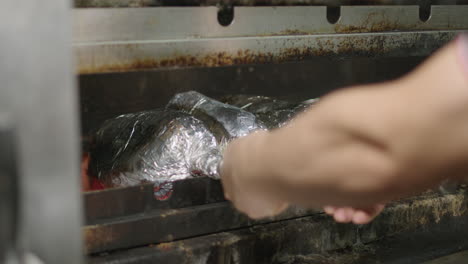 brazilian-barbecue-puts-meat-skewers-covered-in-aluminium-foil-into-the-charcoal-grill