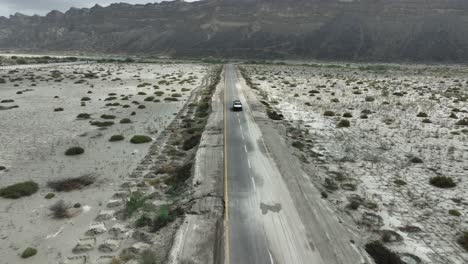 Seguimiento-De-Imágenes-De-Drones-De-Un-Jeep-Desde-El-Frente-En-Una-Carretera-Recta-Entre-El-Valle-Y-La-Montaña-Hingol-Baluchistán