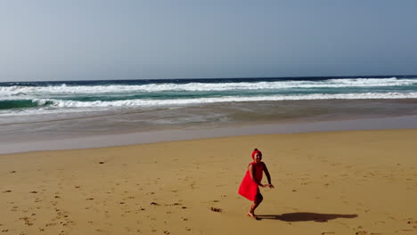 Una-Mujer-Vestida-De-Rojo-Corre-Y-Juega-En-La-Playa,-Fuerteventura