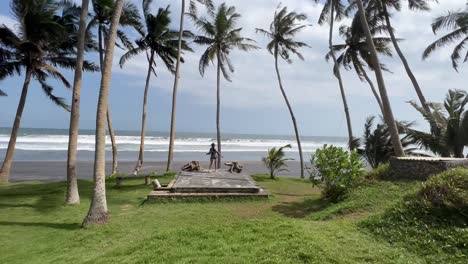 Junges-Mädchen-Im-Strand-Kimano-Schlendert-Zwischen-Hoch-Aufragenden-Kokospalmen-Am-Schwarzen-Sandstrand-Von-Pasut,-Bali