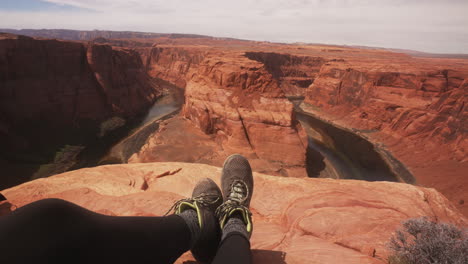 Young-woman-hiker-POV-sitting-above-Horseshoe-Bend-in-the-Grand-Canyon-Arizona,-USA