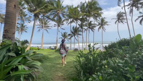 Young-Girl-in-Beach-Kimano-Strolls-Amongst-Towering-Coconut-Palm-Trees-at-Pasut-Black-Sand-Beach,-Bali