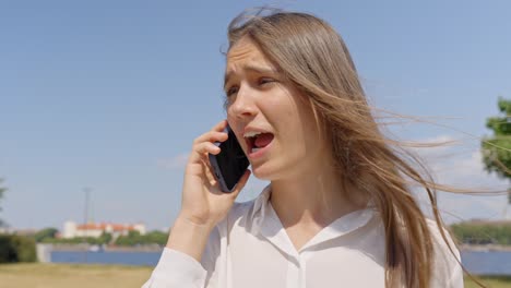 Woman-talking-on-her-smartphone-at-her-ear-outdoors-under-the-sun,-static-closeup