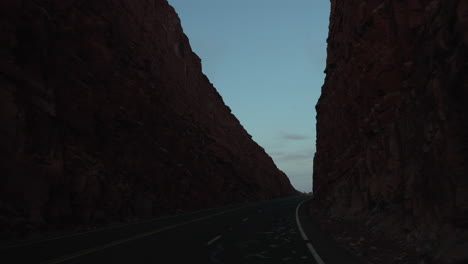 Driving-down-a-desert-road-in-between-tall-rock-walls-at-dusk---Concept:-dark-road,-eerie,-alone,-discovery,-exploration,-roadtrip,-camping