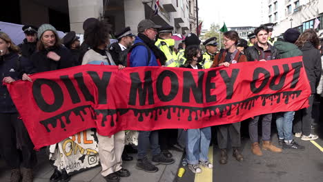 Extinction-Rebellion-activists-hold-a-banner-that-reads,-“Oily-money-out”-while-blocking-the-entrance-to-the-Intercontinental-Hotel-in-Mayfair-where-the-Energy-Intelligence-Forum-is-taking-place