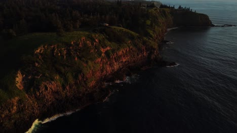 Aerial-parallax-shot-over-the-scenic-coastline-of-norfolk-island-in-australia-with-views-of-the-reddish-rocks-of-the-cliffs-and-the-reflecting-sea-at-golden-hour-on-an-adventurous-journey