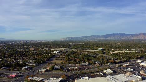 Drone-Aéreo-De-Camiones-A-La-Izquierda,-Toma-De-Paisaje-Extremadamente-Amplio-Del-Valle-Del-Condado-De-Salt-Lake-Cubierto-De-Edificios,-Carreteras-Transitadas-Y-Coloridos-árboles-Otoñales-En-Una-Cálida-Y-Soleada-Tarde-De-Otoño-En-Utah