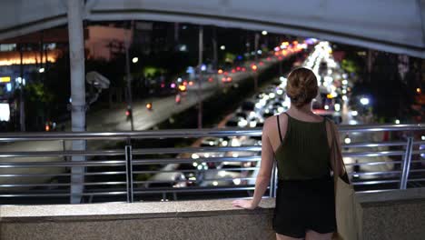 Female-Traveler-Standing-Above-Evening-Rush-Hour-Traffic-In-Bangkok,-Thailand