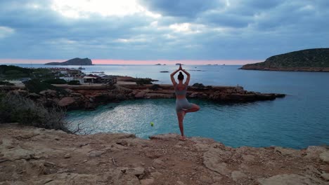 Magic-aerial-top-view-flight-Yoga-Girl-position-tree-sunset-cliff-beach-island-ibiza-Spain-ascending-drone