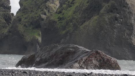 Großer-Felsen-Entlang-Der-Küste-Islands,-Mit-Einer-Welle,-Die-Gegen-Den-Felsen-Plätschert