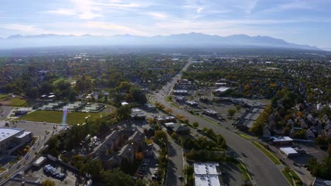Dolly-in-tilt-up-aerial-drone-extreme-wide-landscape-shot-of-the-Salt-Lake-county-valley-covered-in-buildings,-busy-roads,-and-colorful-autumn-trees-surrounded-by-mountains-on-a-fall-evening-in-Utah
