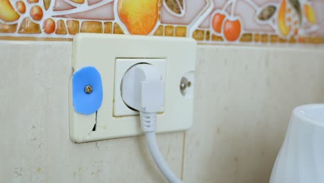 View-at-white-broken-patched-up-electricity-socket-with-plug-in-cable