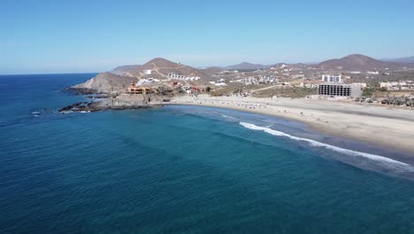 Luftaufnahme-Der-Malerischen-Küste-Am-Strand-Von-Cerritos-In-Baja-California-Sur,-Mexiko-Mit-Ruhigen-Wellen,-Hotelgebäuden-Und-Strandbesuchern-Während-Ihres-Sommerausflugs-An-Einem-Sonnigen-Tag