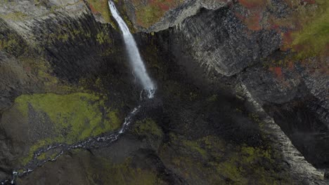 Aerial-tilt-down-shot-of-majestic-waterfall-crashing-down-rocky-cliffs-into-valley-of-Iceland