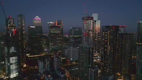 Aerial-view-across-iconic-futuristic-Canary-Wharf-London-high-rise-cityscape-illuminated-skyscrapers-at-twilight