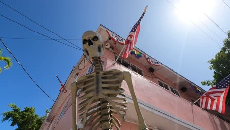 Gruseliges-Skelett-Vor-Festlichem-Rosafarbenem-Gebäude-Mit-US-Flaggen