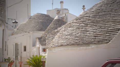 Charming-alley-in-Alberobello-with-white-houses-and-green-plants-and-a-red-car